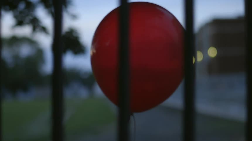 Red balloon floats through a city in the evening
