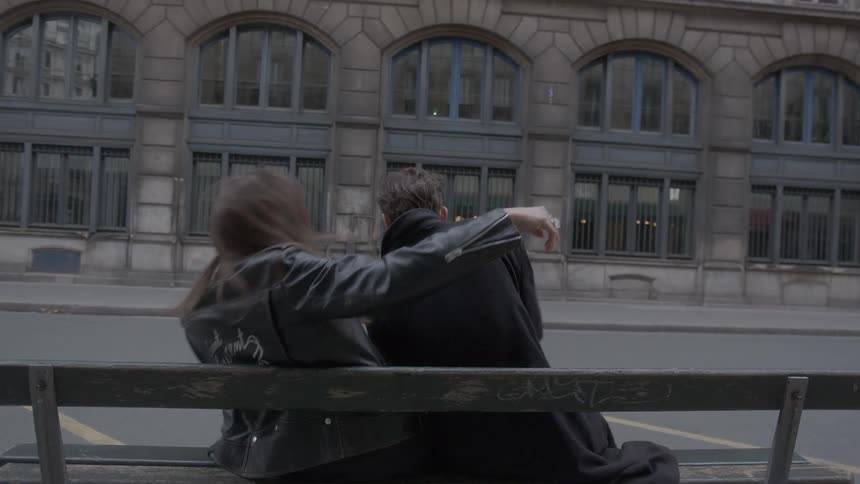 A man and woman collide as they sit together on a bench on the side of a street