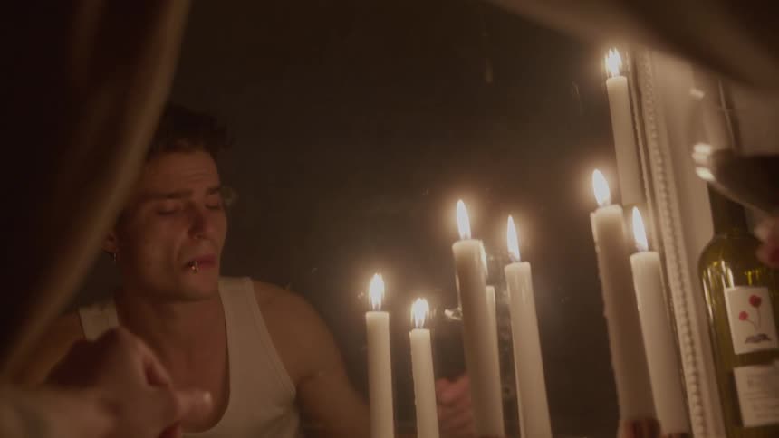 Mirror reflection of a young man smoking and holding a wine bottle by candlelight indoors during night time