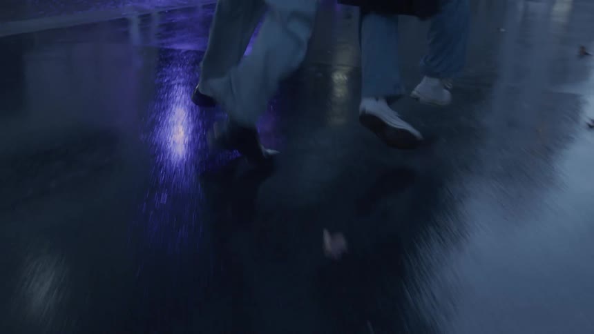 Two people running on a wet sidewalk reflecting city lights