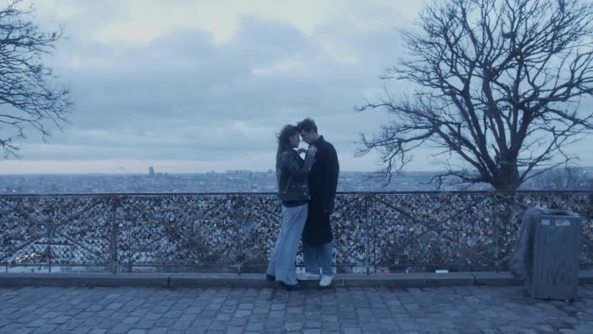 A man and woman are kissing as they stand next to a fence