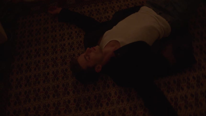 Young man wearing a black jacket lying down with his arms outstretched on the floor indoors
