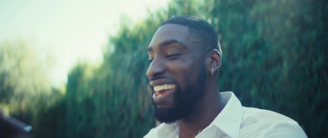 A man sitting at a wood table in a backyard smiles and laughs duting a video call with a tablet as he moves the device around to show off his surroundings