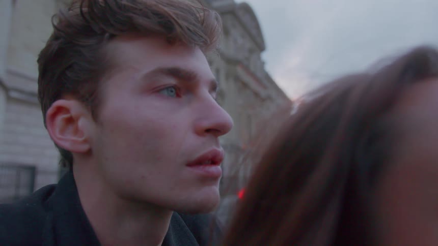Young man and young woman very close to each other looking at a body of water with an urban area on the background outdoors during day time