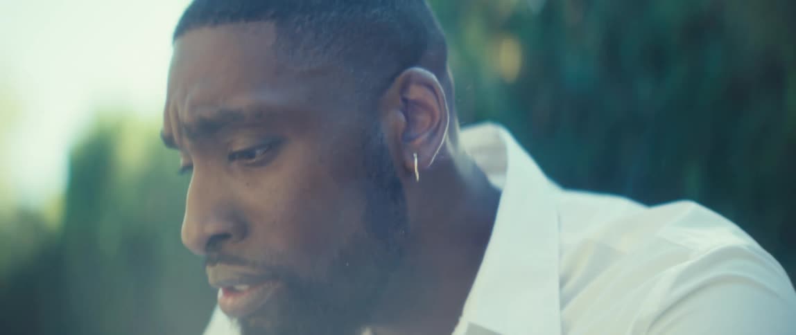 A closeup shot pans from a mans hands holding a phone up to his face in profile as he sits outdoors