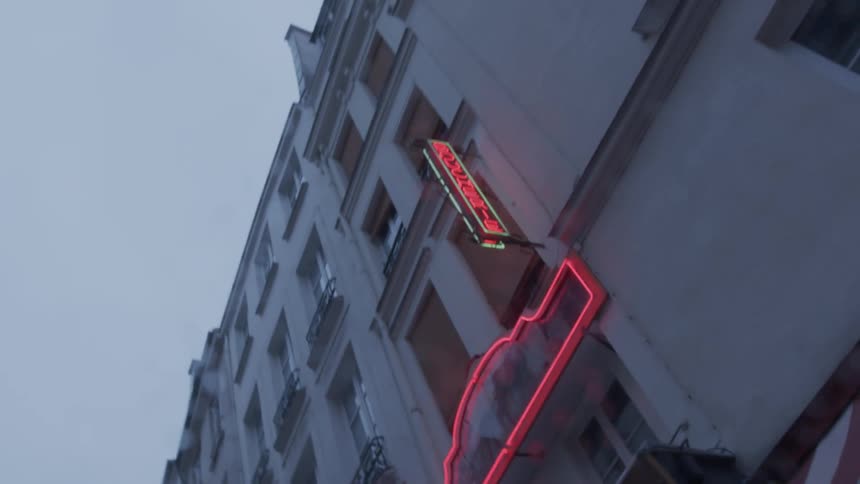 A lowangle shot captures the facade of a tall old apartment building under a gloomy overcast sky emphasizing the height and repetitive windows a vintagestyle neon sign with a red outline and vertical green letters reading botique is affixed to the
