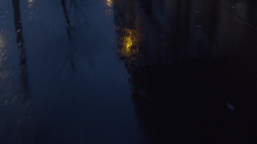 A street wet from rainfall at night with streetlights reflecting on the surface