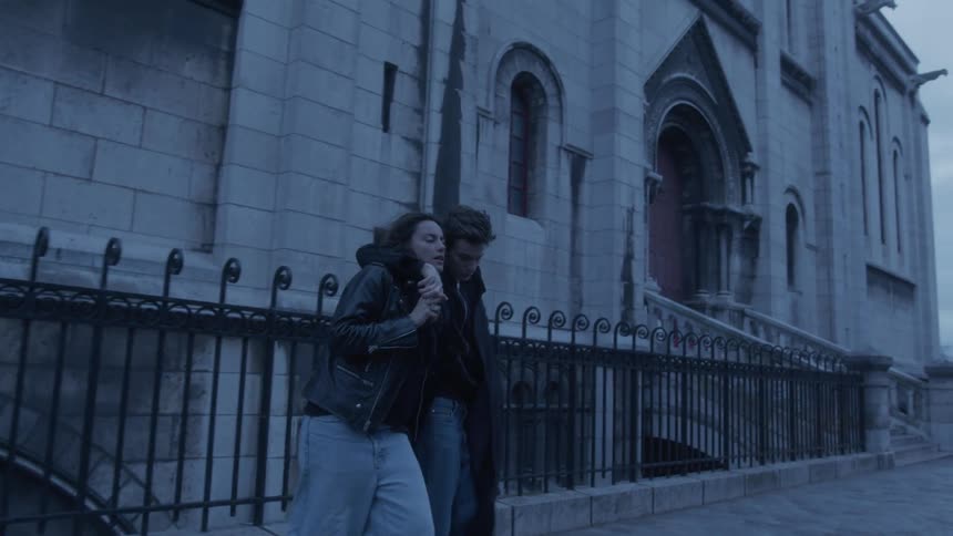 The couple hug while walking past the stone building