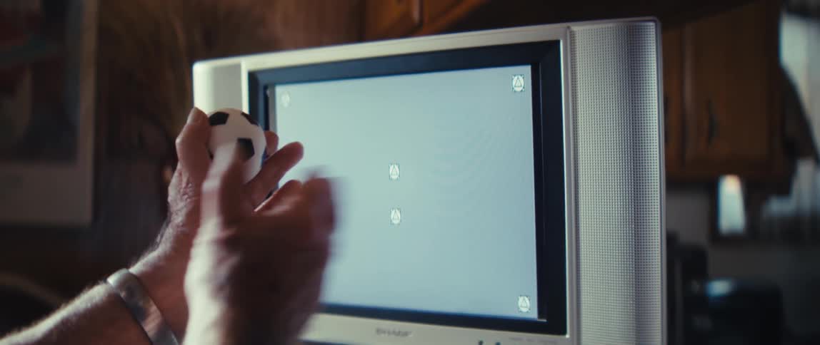 Hand holds a soccer ball in front of a television screen displaying