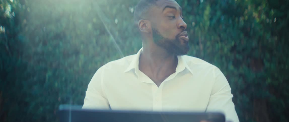 A man in a backyard holds a tablet in front of him smiling as he uses it to make a video call then moving it around to show his surroundings