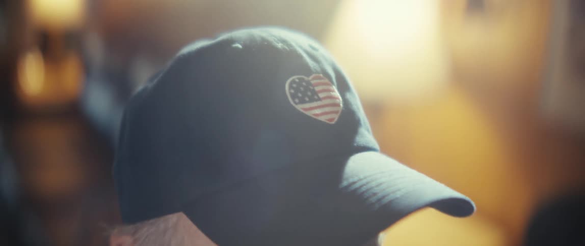 An elderly man with a blue cap with a heart shaped american flag in the front