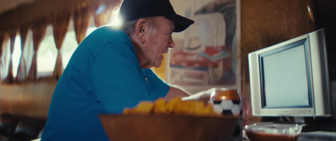 The man is waves and claps his hands at the sports game on his television