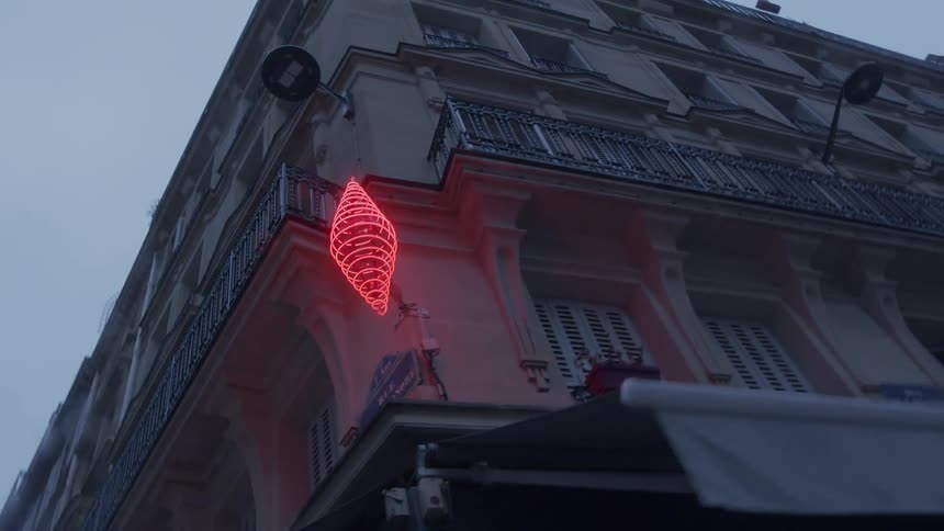 A corner of a europeanstyle building glows with a red neon spiral sign under an overcast sky