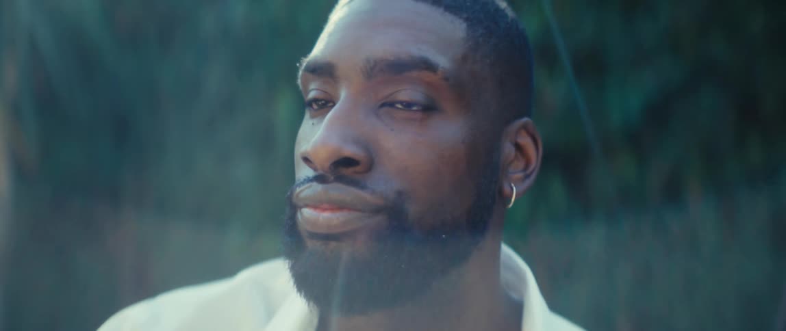 A man sitting in a backyard makes a pensive expression shakes his head then frowns and continues pondering