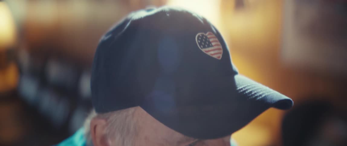 The man is wearing a baseball cap with a heart logo on it