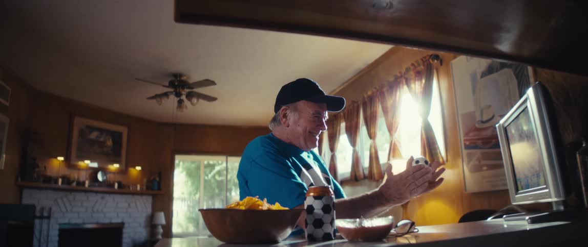 An elderly man is beaming with joy and clapping his hands while watching television