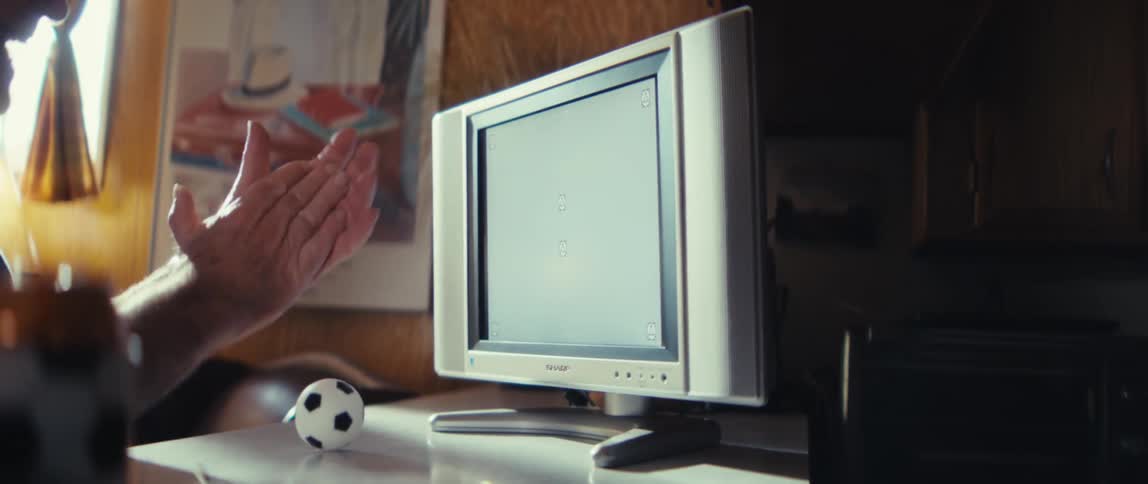 Elderly man in a baseball cap is watching television with great enthusiasm