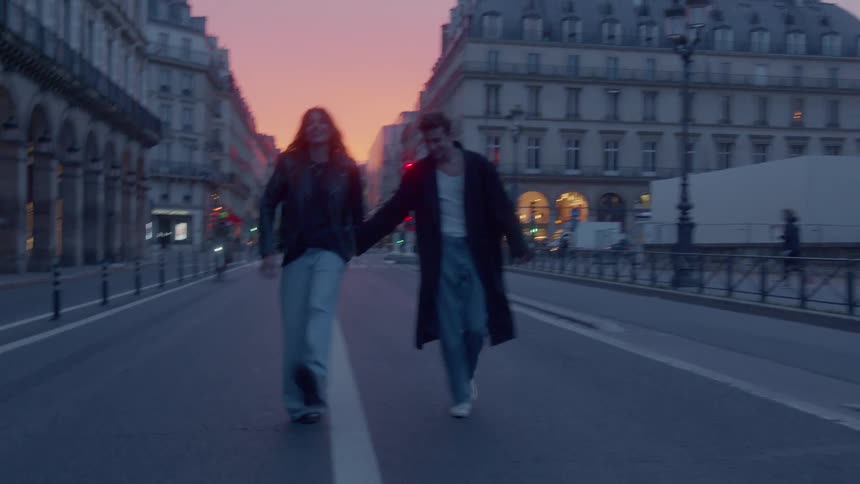 The couple hold hands while walking on the road in the city