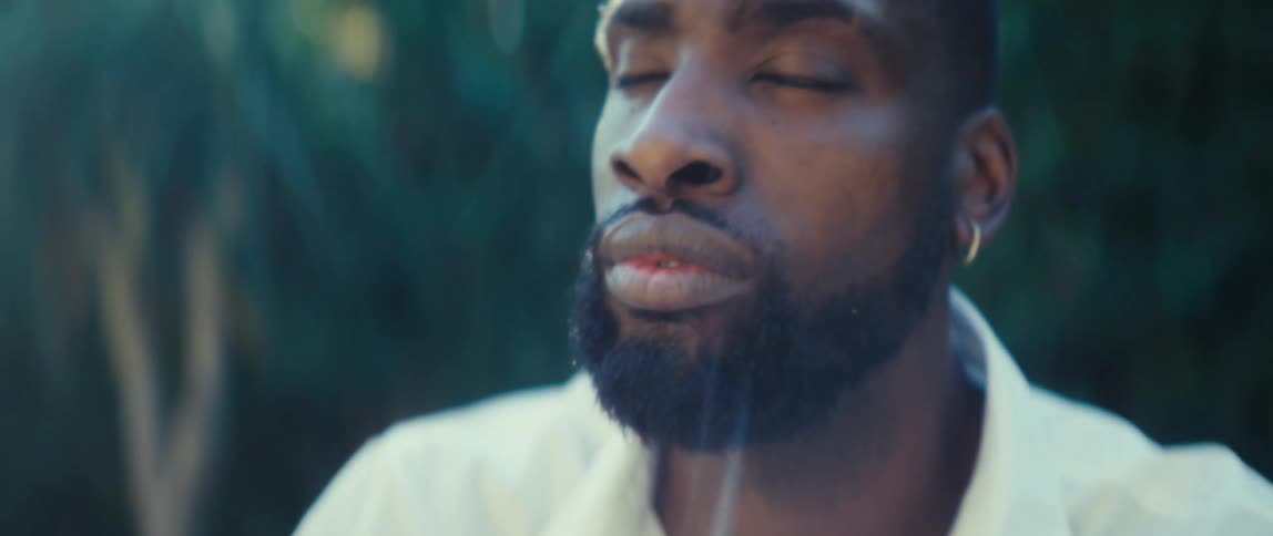 Bearded black man wearing a white shirt texting on a smartphone with a contemplative face expression before smiling and nodding outdoors during day time