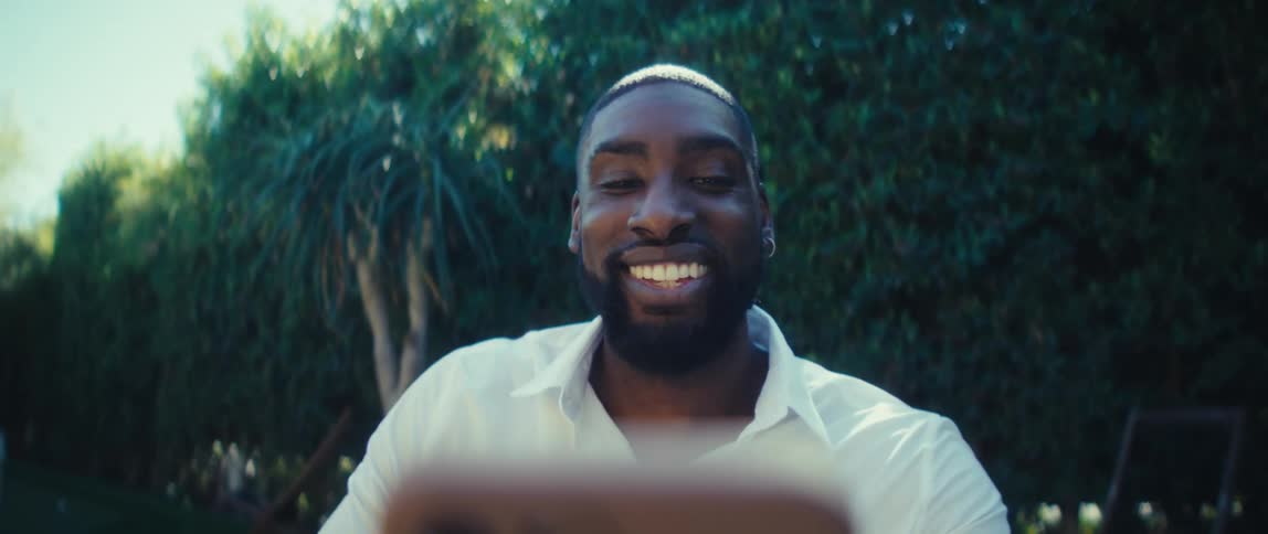 A man in a backyard smiles and waves while on a video call on his smart phone