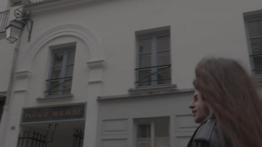Couple in black jackets walks together in front of a white and maroon facade with barred windows