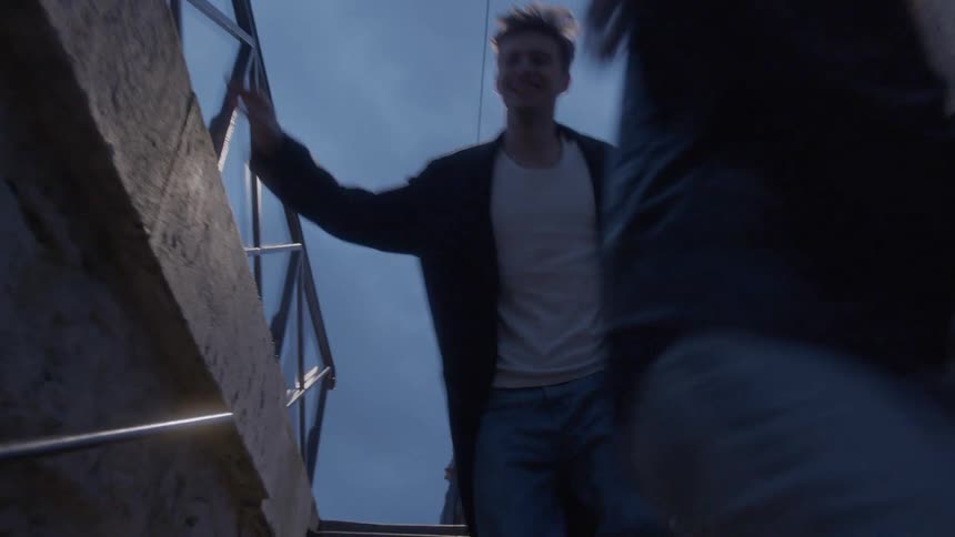 A couple climbs an outdoor stairwell at dusk beneath a glowing lamp