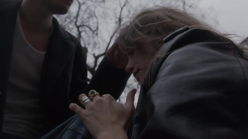 Woman leans against a male knee as the man leans forward to hug her head as they sit outdoors on a winter day
