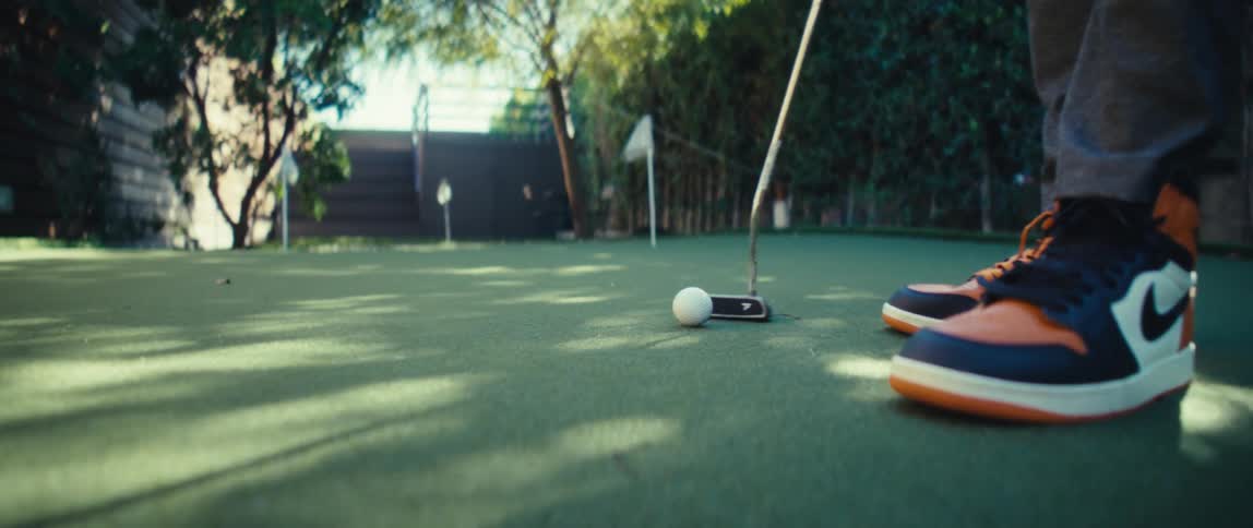 A person in tennis shoes practices putting a golf ball on artificial turf