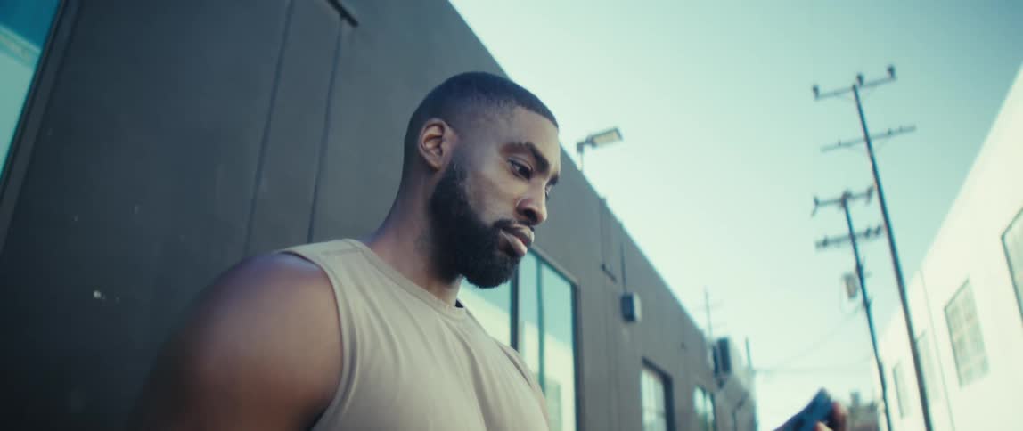 Man stands outside next to a building looking at his phone in his hand
