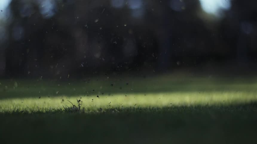A closeup slowmotion shot shows a golf club hitting a ball sending a large divot of grass and dirt exploding into the air