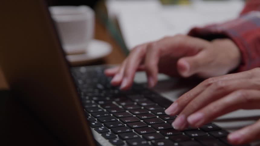 A persons fingers typing rapidly on a laptop keyboard with black keys