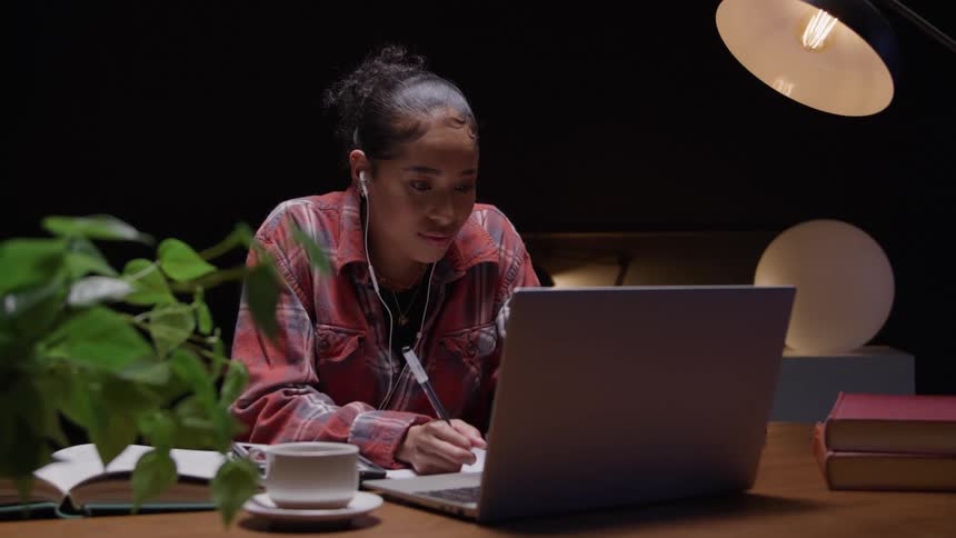 A young black woman studying with a laptop computer at a table in a room at night