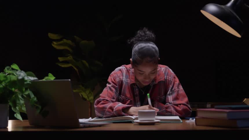 A teenager has a cup of coffee in front of her as she writes in a book