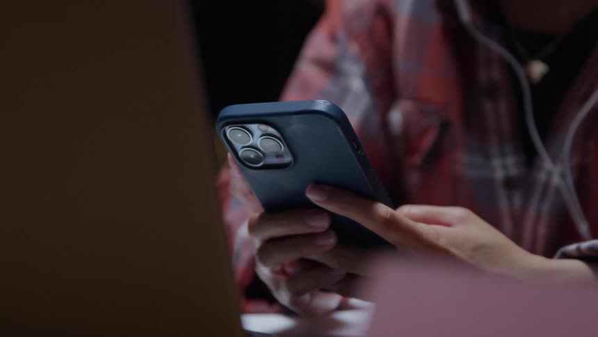 Person holds a smartphone while working in front of a laptop