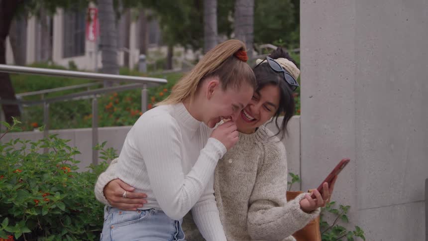 Friends laugh together while looking at something funny on the phone