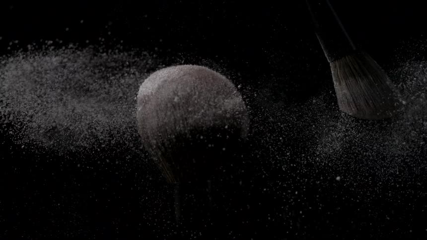 A paintbrush being passed over the bristles of another paintbrush releasing various powder particles