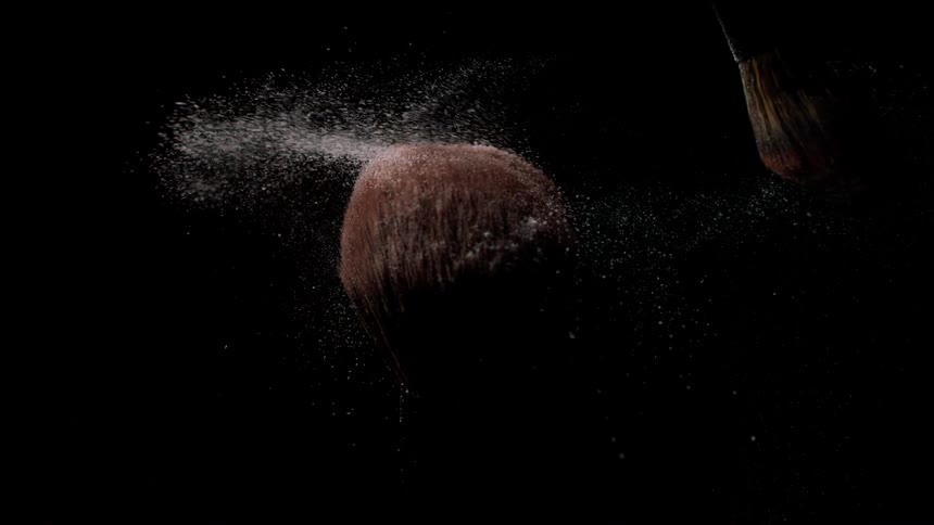 Makeup brush releases powder softly into the dark air