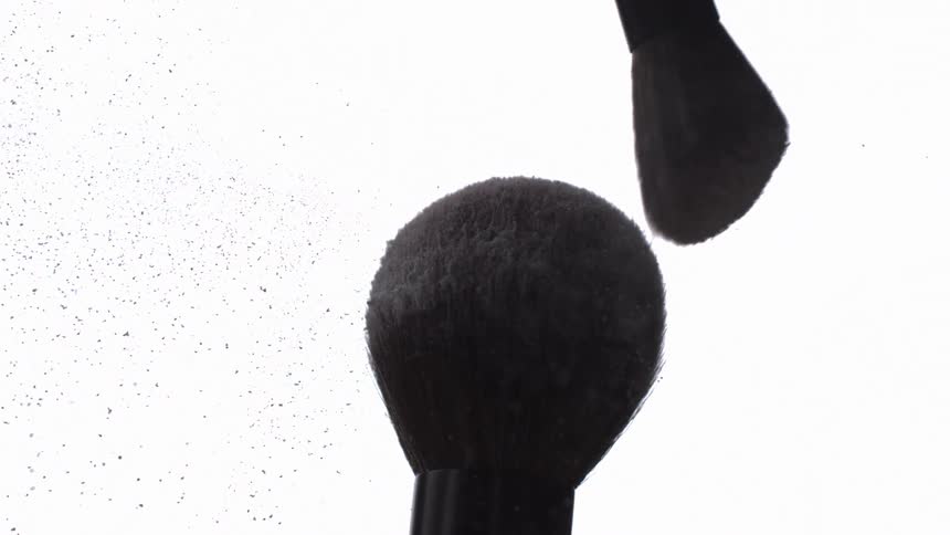 Makeup brush swings into another brush and powder flies into the air
