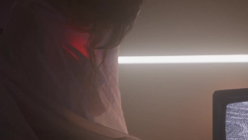Person wrapped in fabric gazes at intense red light near the chest