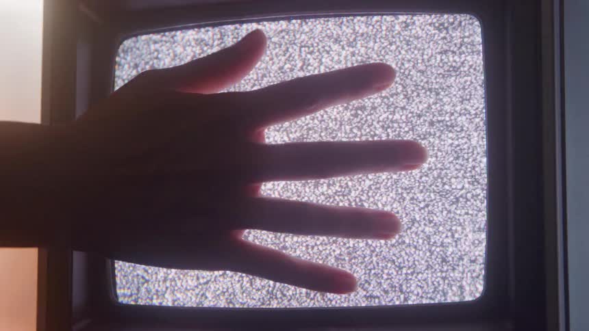 Hand touches the screen of a glowing static tv