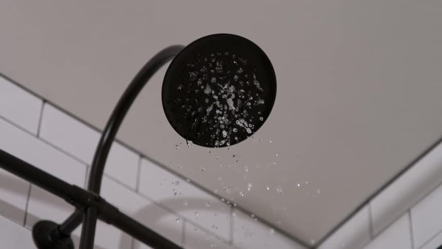 Water is slowly dripping from a showerhead in a bathroom