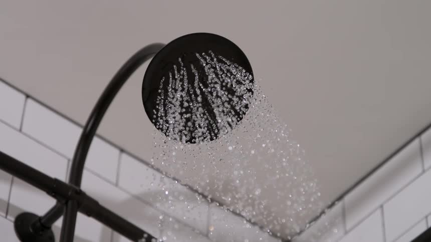 Stream of water falling from a black showerhead in operation
