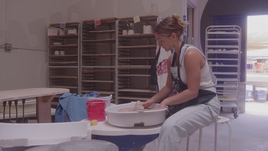 Woman puts a piece of clay on a potters wheel in her workshop during the daytime