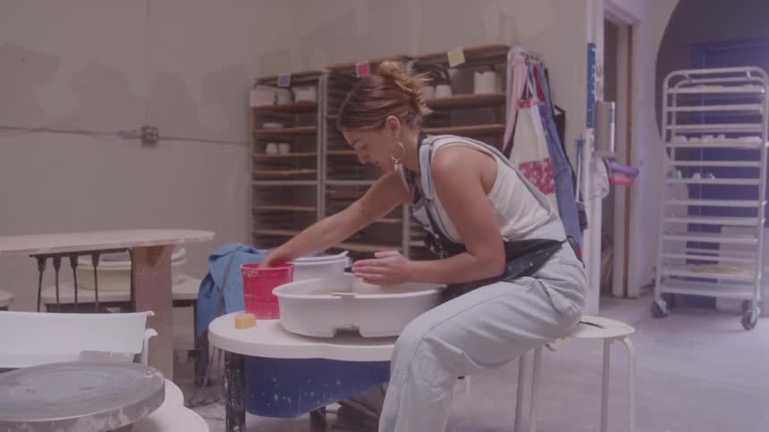 Woman shaping clay on a pottery wheel inside a studio