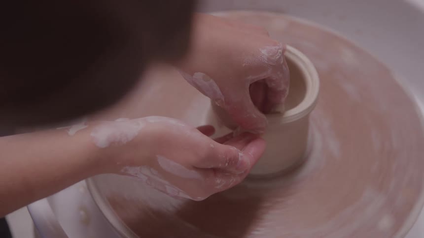 Female potter shapes clay on a potters wheel