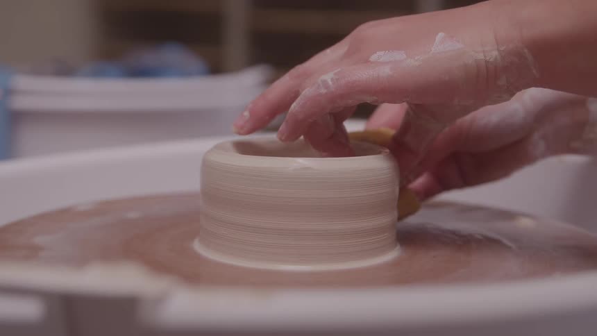 Hands shaping wet clay on a spinning pottery wheel