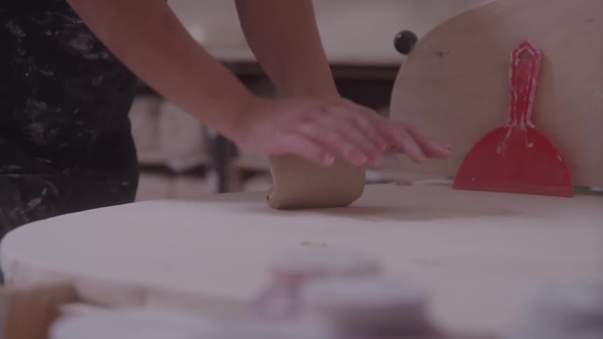 Female potter kneads clay on a table in her workshop