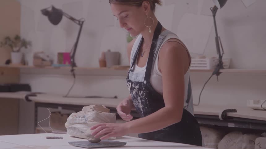 Female potter standing in her workshop weighs a roughly shaped clay ball