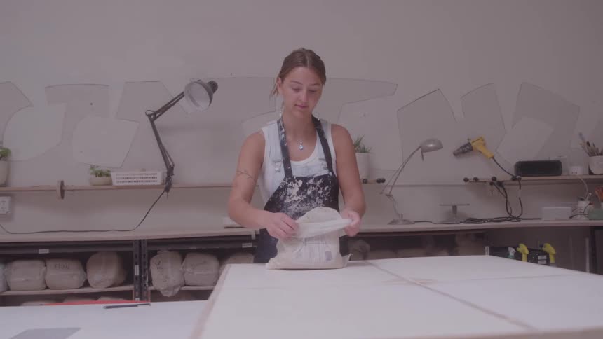 A woman is unwrapping clay in an artist studio