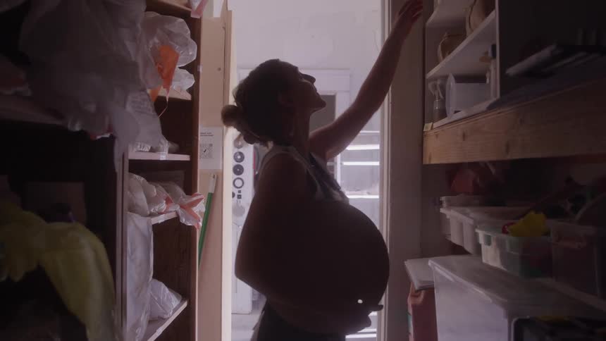 A female wearing an apron enters a supply closet for pottery items and grabs two items